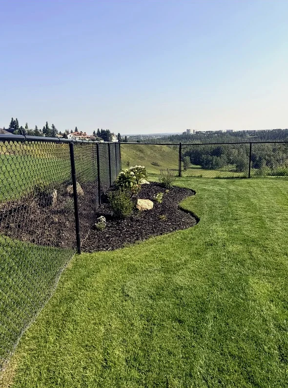 Same ridge fence line with a new curved mulch bed, boulders, shrubs and fresh lawn by Edge Property Services