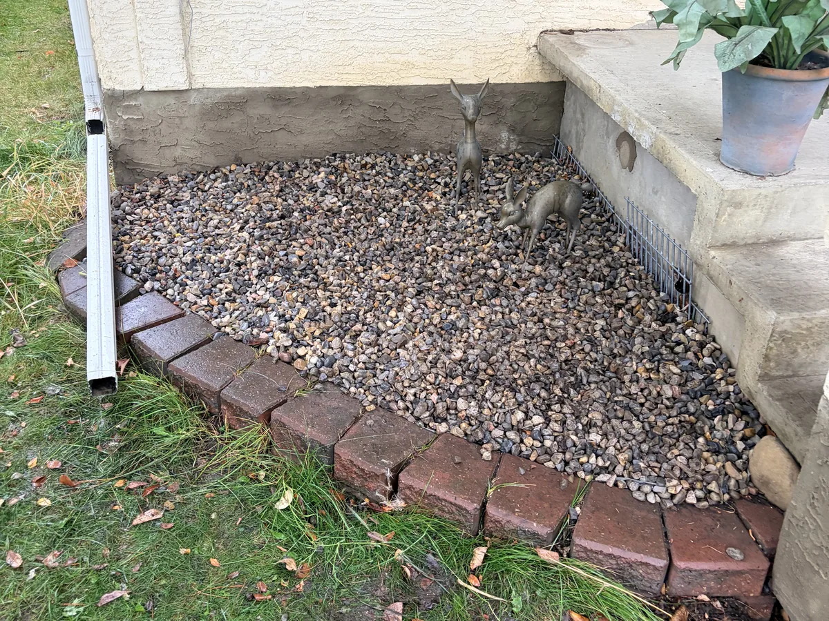 Finished decorative rock in a compact corner bed beside concrete steps and a curved brick border