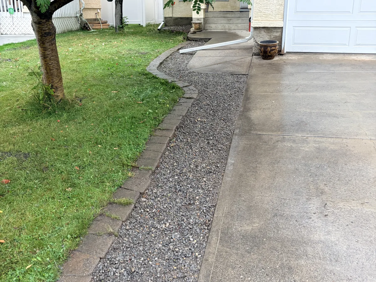 Long decorative rock border following a driveway toward the house beneath a mature tree